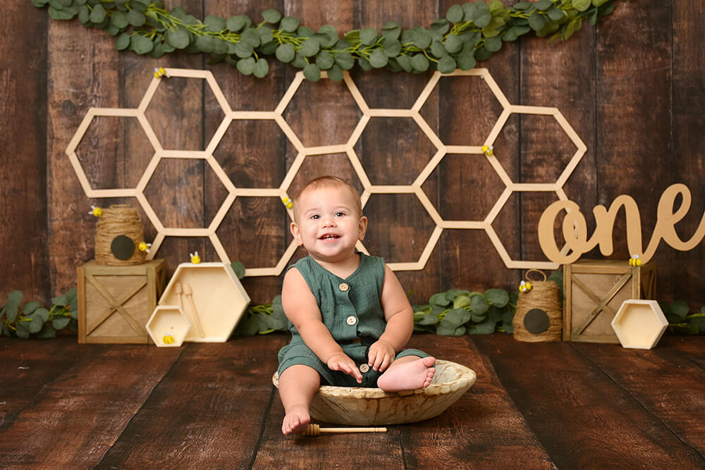 boy at his first birthday photoshoot in houston smiles in front of a wooden rustic bee setup